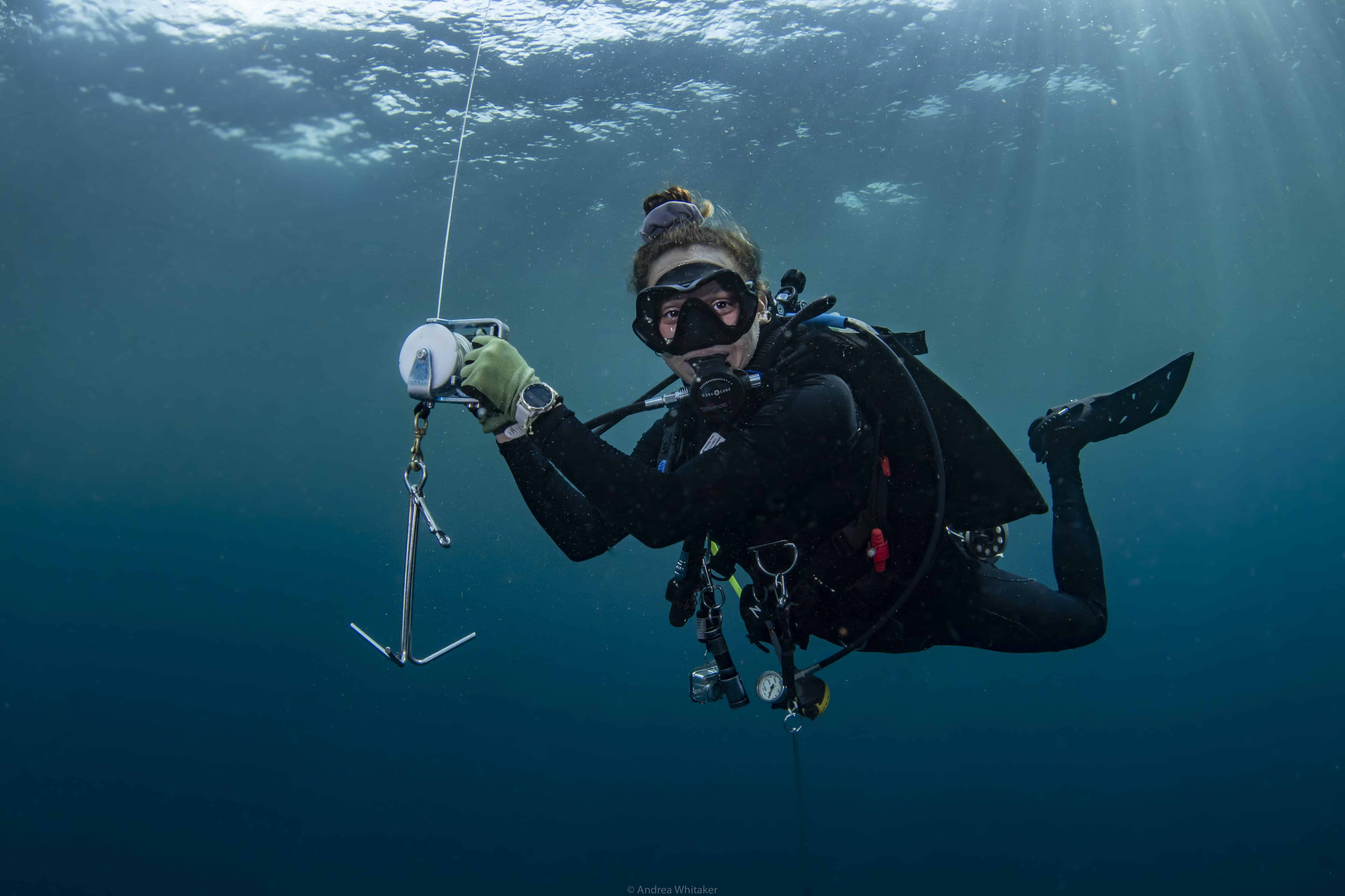 A diver hangs at her safety stop holding onto a line and reel